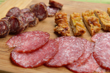 Different meat products (sausages, salami, breaded chicken breast) arranged on a wood trencher. Rustic food. Selective focus
