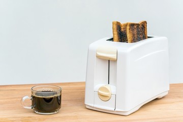 Black coffee in clear cup and Toaster and burnt toasts on wooden table with copyspace