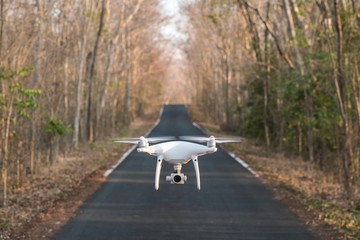 Quadcopter drone flying on the tarmac road with trees background..
drone flies with mounted digital camera for video and photo productions