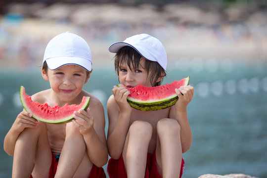Two little children, boy brothers, eating watermelon on the beach