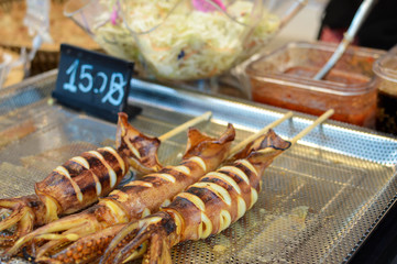 Fototapeta na wymiar Barbecue squid skewers sold from the stalls at a street food market near Central World mall in Bangkok, Thailand