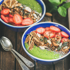 Healthy breakfast. Green smoothie bowls with strawberries, granola, chia and pumpkin seeds, dried fruit and nut in wooden tray, selective focus, square crop. Raw, detox, diet food concept