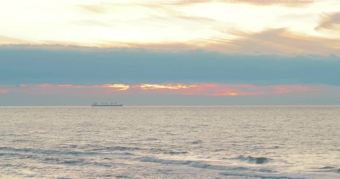 The balker stands at anchor amid a beautiful sunset sky. Stormy sea, waves, wind, colorful clouds