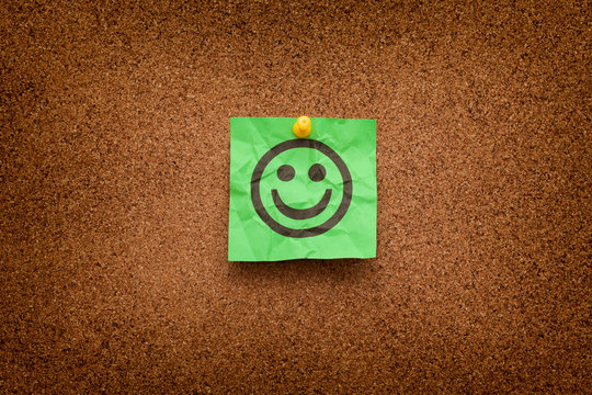 Crumpled Green paper with smiling face on corkboard