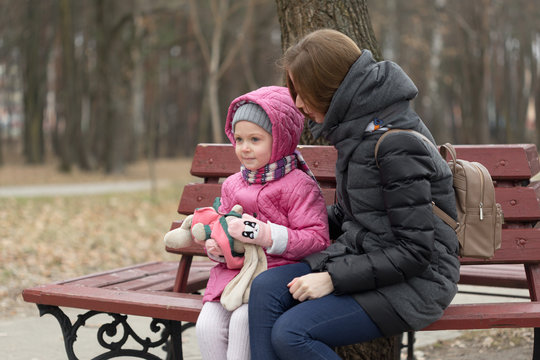 Mom and daughter are sitting on a park bench