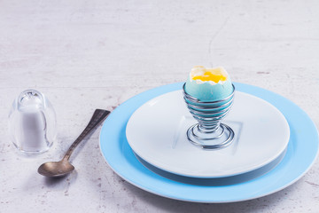 blue easter egg with yellow yolk, spoon - easter breakfast concept