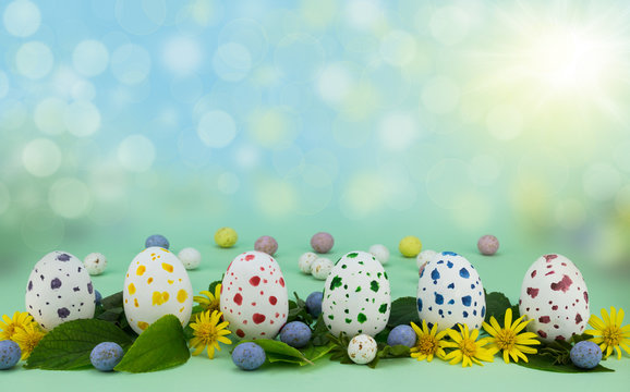 Row of painted speckled chocolate eggs isolated on green background with leaves and flowers