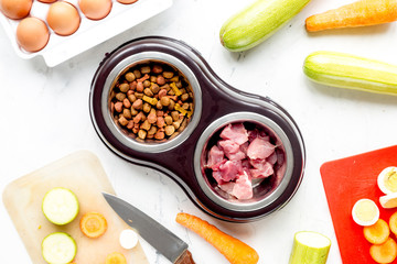 Bowl of dry dogfood, carrot, courgette and meat table background top view