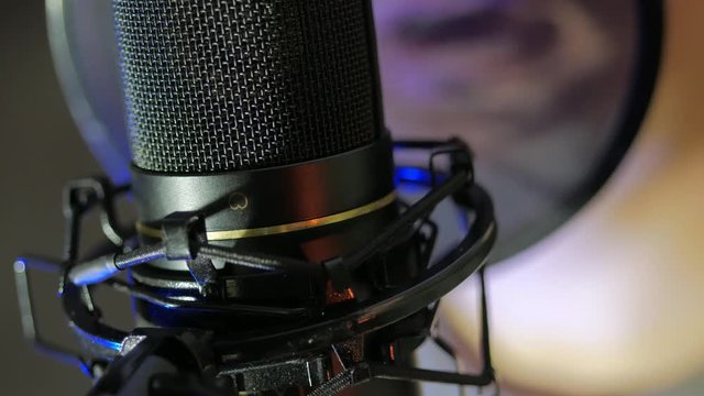 A young man sings a song near a microphone in a recording studio under natural light