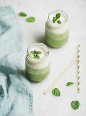 Obraz na płótnie Canvas Ombre layered green smoothies with mint in glass jars over light grey background, selective focus. Clean eating, vegan, vegetarian, weight loss, healthy, diet food concept