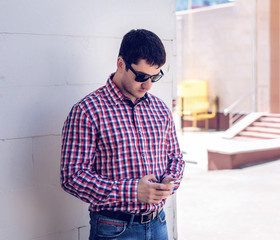 man in  shirt and jeans  sunglasses, holding  mobile phone, read the conversation messages on your , the concept of summer,  businessman  vacation. City lifestyle.