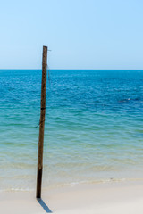 Old Wooden post stuck in white sandy beach.