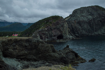 Fototapeta na wymiar Cliffs and Red House along a Rugged Coastline at Lark Harbor in Newfoundland, Canada