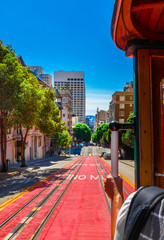 Ride with the cable car in San Francisco. The picture shows a person riding on the famous MUNI train on Powell-Mason line down the hill of Powell Street in San Francisco, California. - obrazy, fototapety, plakaty