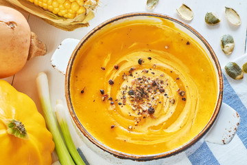 Pumpkin, squash and corn cream soup (puree) with pumpkin seeds on a napkin over white table. Close-up. 