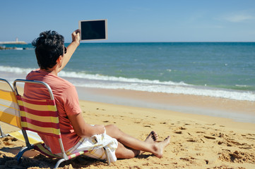 Back view of business man sitting and working with tablet computer on sunny beach outdoors...