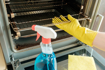 Man's hand in glove with rag cleaning oven