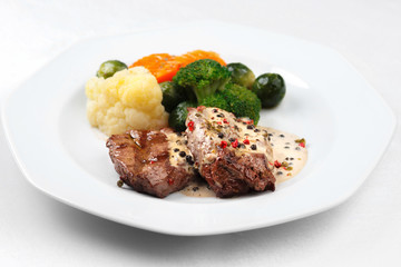 Grilled meat and steamed vegetables in a white plate