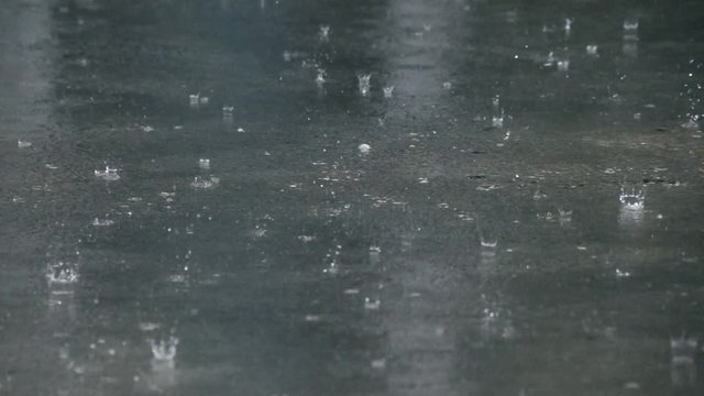 Large raindrops falling on wet concrete during storm