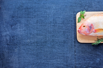 Raw red fish (Nile tilapia) on a wooden board. Dark background. Space for text.