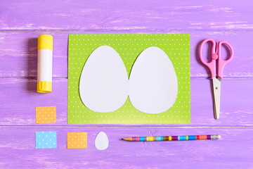 How to make Easter egg greeting card. Step. Tutorial. Colored cardboard sheets, template in shape of egg, scissors, glue stick, pencil on a wood table. Kids Easter paper crafts idea. Top view. Closeup