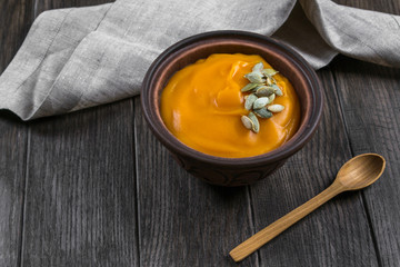 Pumpkin cream soup in a clay bowl on dark wooden  table