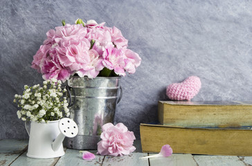 Pink carnation flowers in zinc bucket and book on old wood