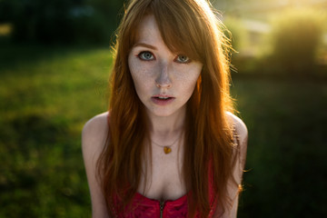 Portrait of a young red-haired girl on a background of greenery in the sunset light