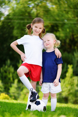 Two cute little sisters having fun playing a soccer game on sunny summer day. Sport activities for children.