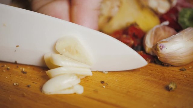 Close up cut garlic over wooden cutting board with knife, chile and pepper on background
