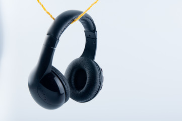 Black headphones hang on rope isolated on white background