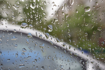 Drops of rain on the car glass with blurred trees on the background