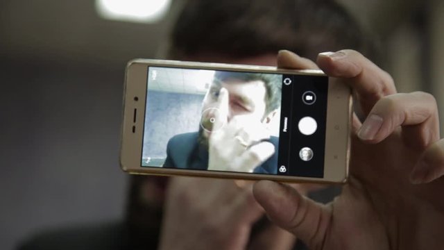 Busy office worker cranks and looking into phone camera. funy businessman picks finger in nose, strokes his beard