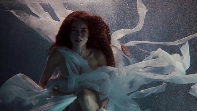 young woman swimming underwater in a white dress like a fairy tale