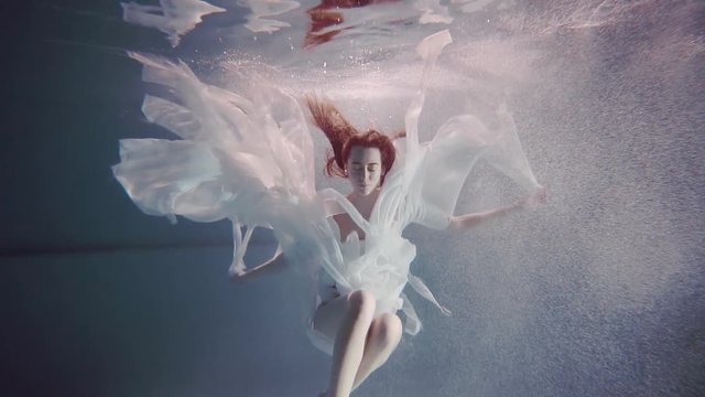 young woman with long red hair swimming underwater like a fairy tale