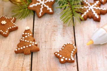 Gingerbread christmas cookies with decorating pen, green pine branch needles with bell and angel on wooden background