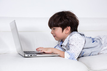 Happy Asian Chinese little boy playing laptop on the couch