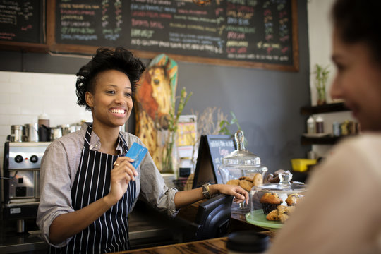 Smiling bartender with credit card and customer in cafe
