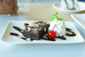 Chocolate brownie cake with whipped cream and cherry on plate.