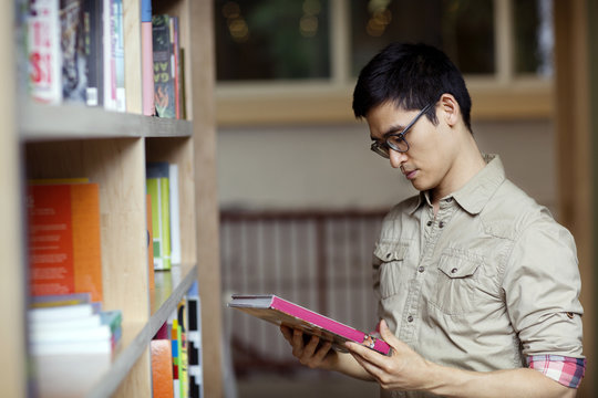 Man looking at book while standing by library shelf