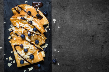 Crepes with blueberries almond flakes and chocolate sauce on black.