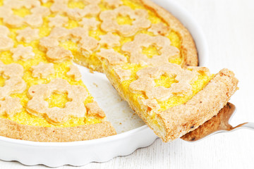 Closeup piece of homemade shortcake on white baking form. Italian crostata with orange and apple filling. Shallow focus.
