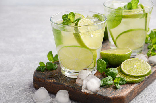 Cold refreshing summer drink with lime and mint in a glass on a grey concrete or stone background. Selective focus.