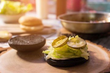 Black burger bun with lettuce. Sauce and pickled cucumber slices.