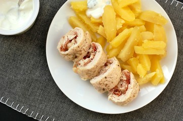 Rolled chicken fillet with prosciuto and mozzarela with pototoes on white plate on grey cloth