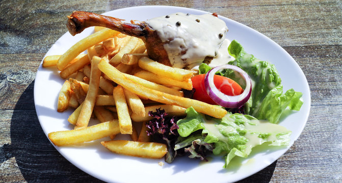 Gourmet food of crispy duck leg confit covered with pepper sauce, with potato fries and lettuce, tomato, onion, on a white plate