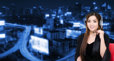 portrait of asian woman support phone operator or call center in headset sitting on red chair on blurred night city background, customer support and service concept.
