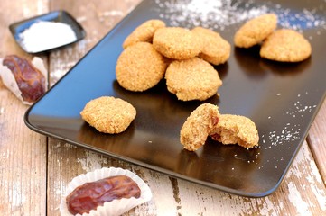 Gluten free cookies with coconut and dates on black plate on wooden background