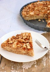 Cake with apples, cinnamon and walnuts on white plate on wooden background