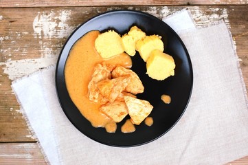 Chicken fillet on sweet pepper with creamy sauce with polenta dumplings on black plate on wooden background